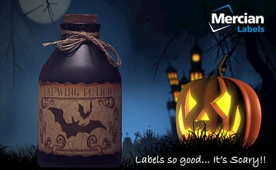 Picture of a bright Jack o Lantern / Carved Pumpkin in the foreground of a graveyard with an internally lit haunted mansion in the background on a dark night with a full, but shaded moon, with an old, short but stout glass bottle in the foreground with a label on it saying Bat Wing potion and text to the side saying ‘Labels so good… It’s scary!!’