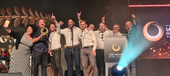 Mercian Labels and supply chain team celebrating on stage and holding the trophy after being announced as Winners at The Label Industry Global Awards 2023.